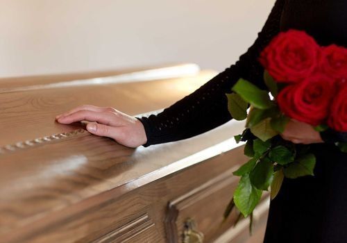 Una mujer sostiene un ramo de rosas rojas y está de pie junto a un ataúd.