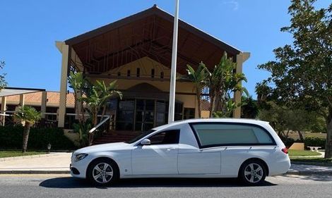 Un coche fúnebre blanco está estacionado frente a una iglesia.