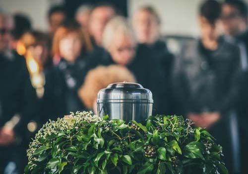 Un grupo de personas están de pie alrededor de una urna en un funeral.