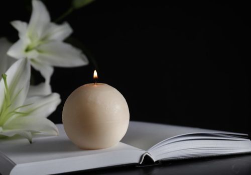 Una vela está encima de un libro abierto al lado de flores.