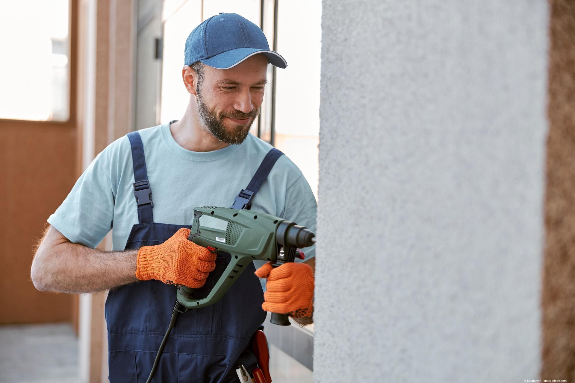 Handwerker mit Schutzkleidung benutzt eine Bohrmaschine an einer Wand.