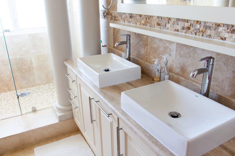 Meuble-lavabo moderne avec deux vasques blanches et robinetterie chromée, à côté d'une douche carrelée.