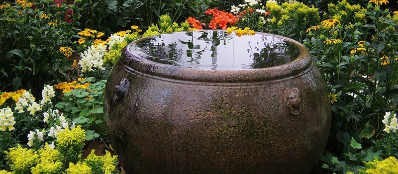 Fontaine ronde en pierre dans un jardin fleuri aux fleurs jaunes, blanches et orange