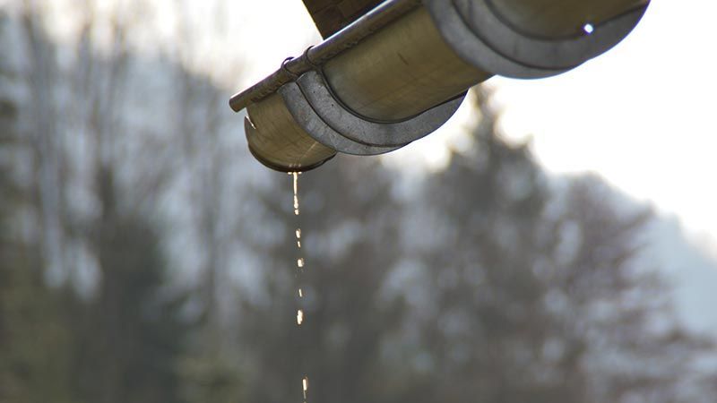 Gouttes d'eau d'une gouttière en métal gris sur un fond hivernal flou