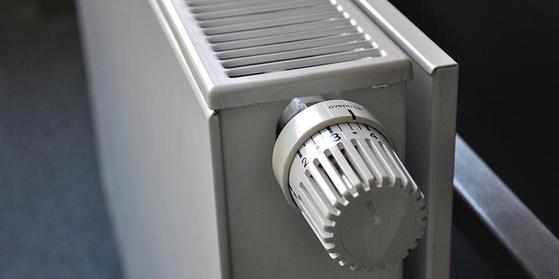 Gros plan sur un radiateur argenté avec un bouton de commande thermostatique blanc