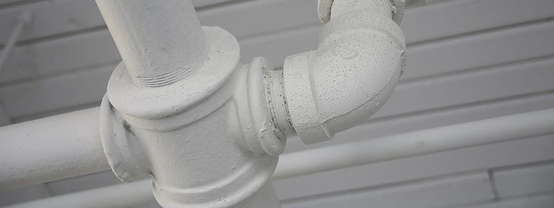 Tuyauterie industrielle blanche et vanne au plafond sur fond gris clair