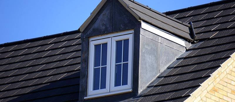 Lucarne sur un toit d'ardoise grise à encadrement blanc se détachant sur un ciel bleu