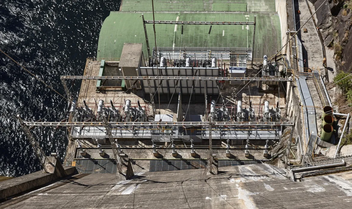 Vista aérea de una central hidroeléctrica situada sobre una presa, con su equipamiento eléctrico. El agua rodea la presa.