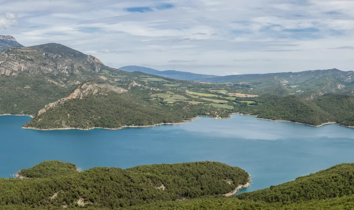 Paisaje de lago de montaña con agua azul y verdes colinas boscosas bajo un cielo nublado.