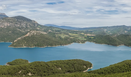Paisaje de lago de montaña con agua azul y verdes colinas boscosas bajo un cielo nublado.
