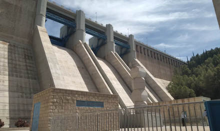 Una gran presa de hormigón con múltiples aliviaderos recortada contra un cielo nublado.