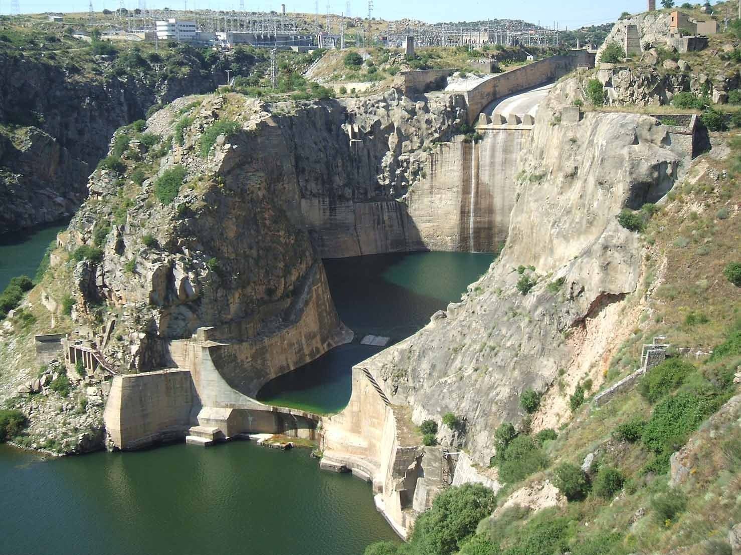 Presa con agua que cae en cascada, rodeada de acantilados rocosos y agua verde.