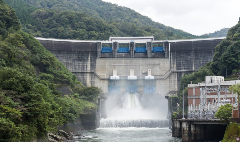 Presa liberando agua; exuberantes montañas verdes enmarcan la estructura.
