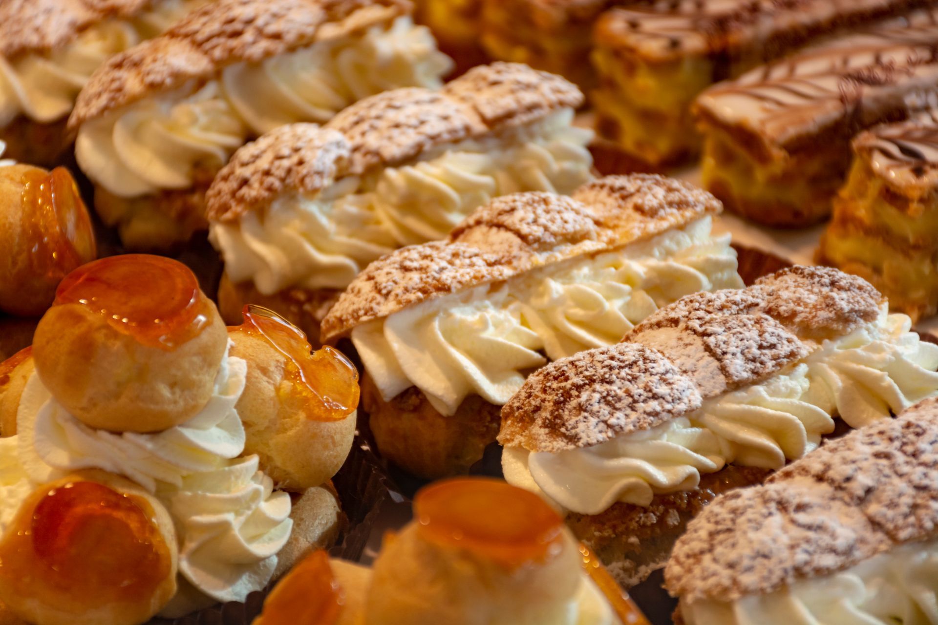 Une présentation d'éclairs fourrés à la crème et de choux saupoudrés de sucre glace dans un décor de boulangerie.