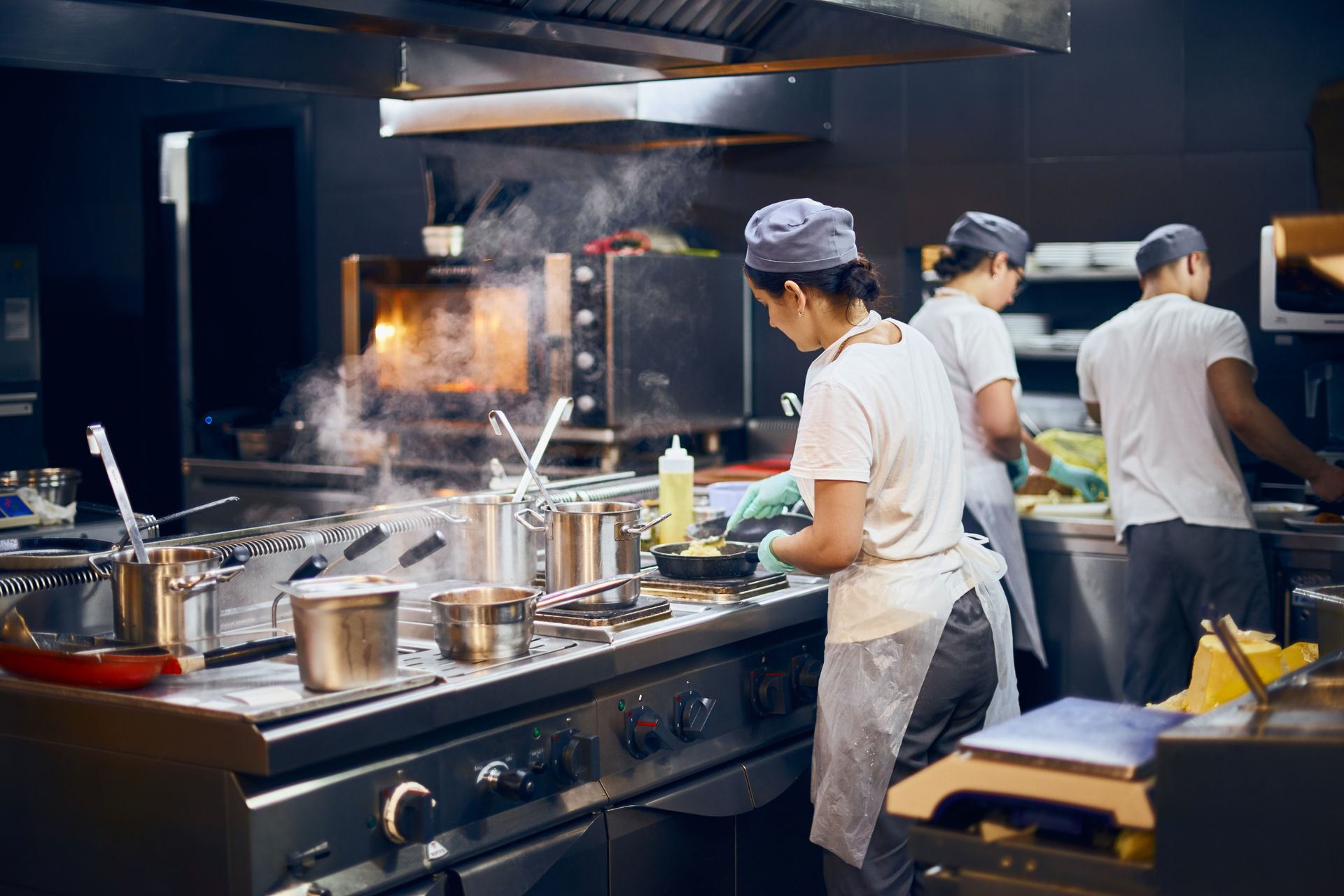 Trois employés de cuisine, vêtus d'uniformes et de toques, travaillent aux fourneaux dans la cuisine d'un restaurant.