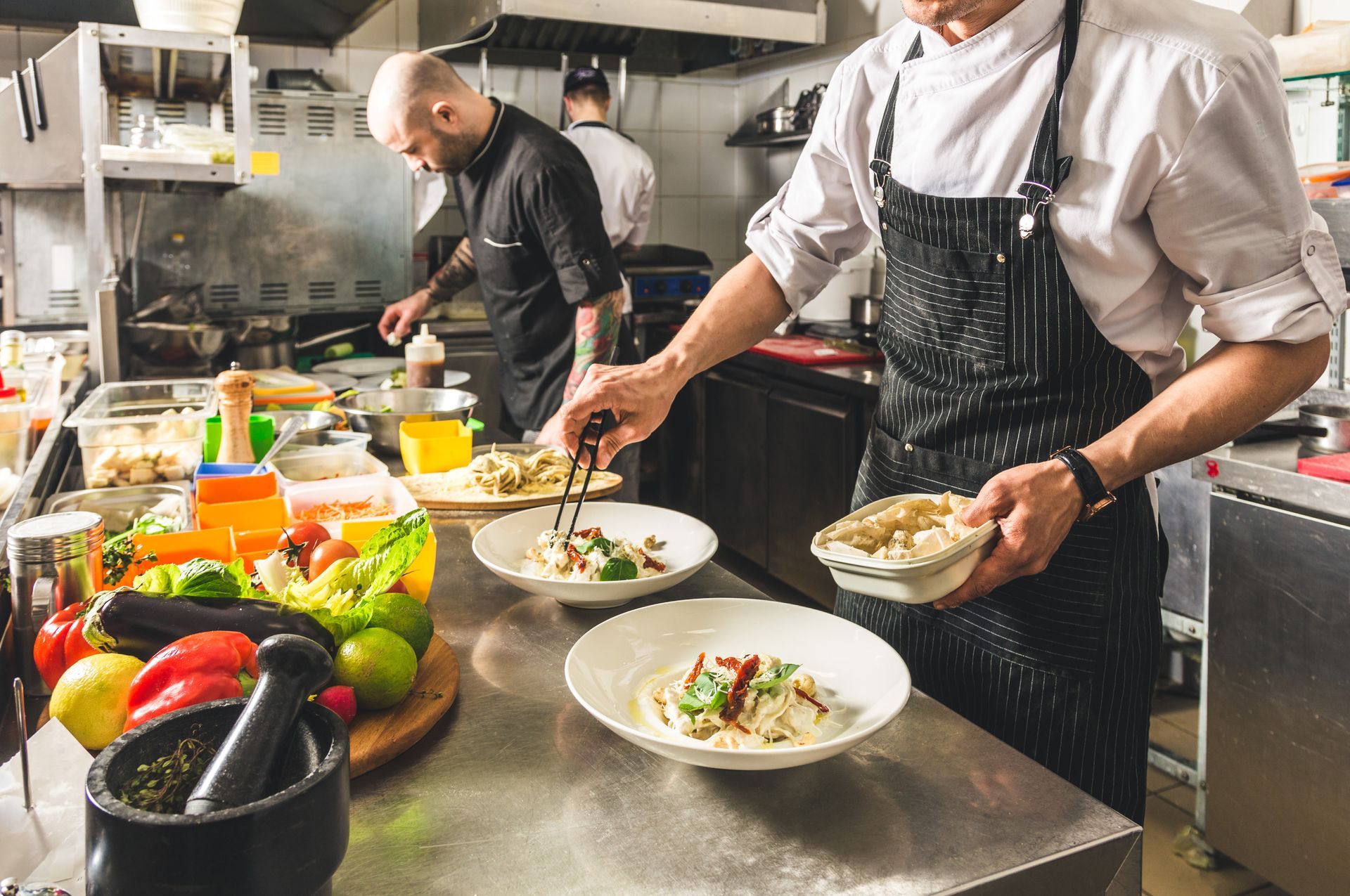 Deux chefs préparent des plats dans une cuisine professionnelle, dressant les assiettes au milieu de produits frais.
