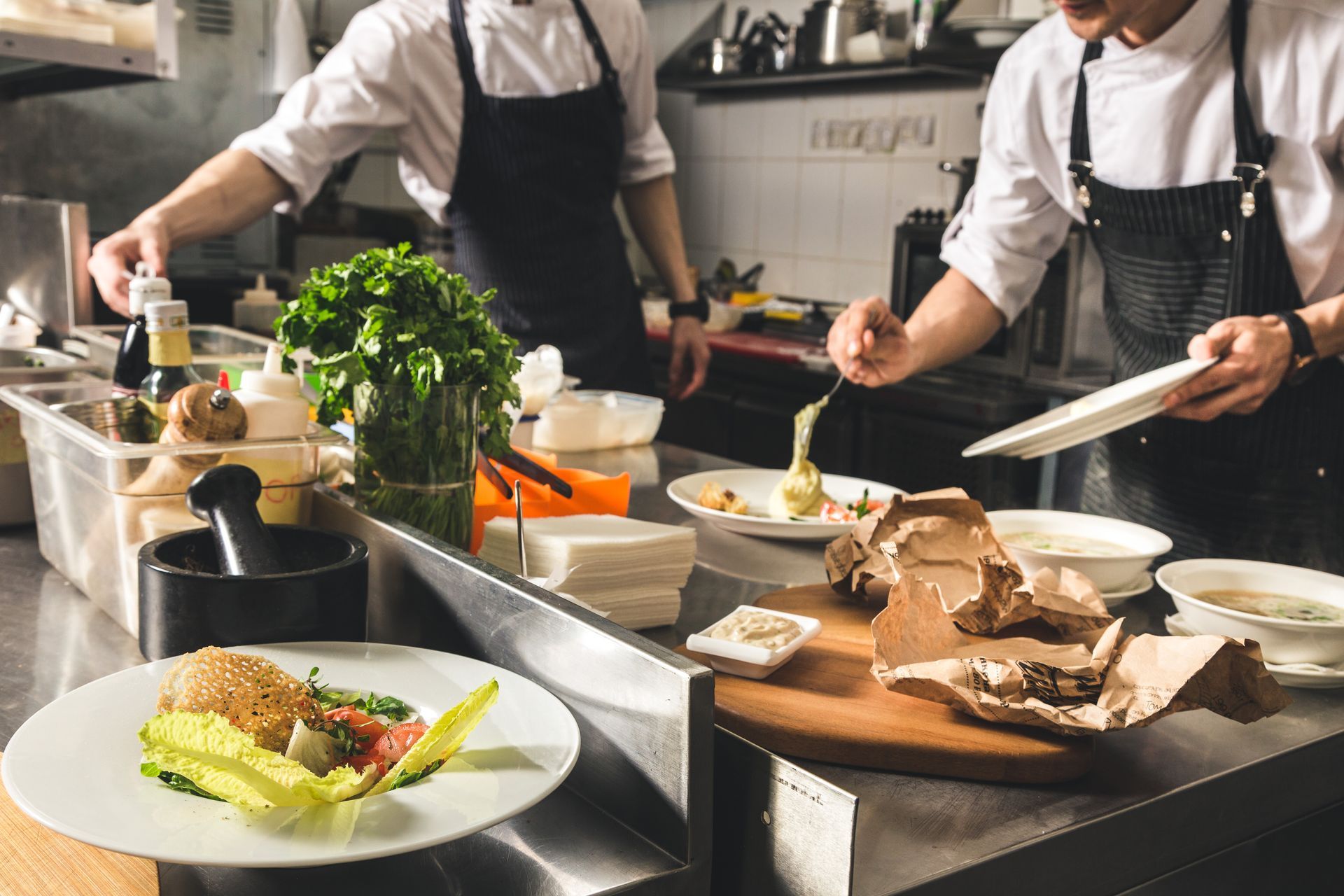 Deux chefs en blouse blanche et tablier noir préparent et dressent des plats gastronomiques.