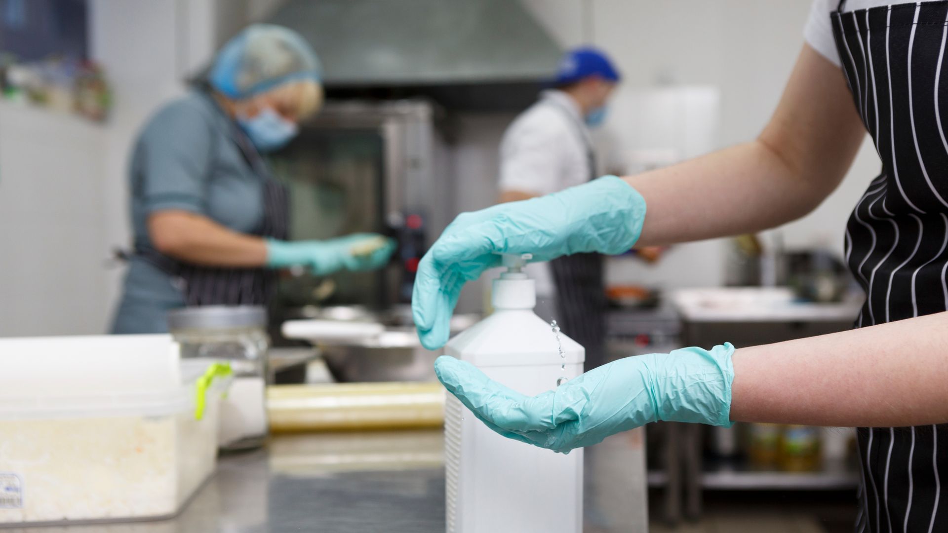 Une personne portant des gants se verse du gel hydroalcoolique dans les mains, tandis que d'autres travaillent.