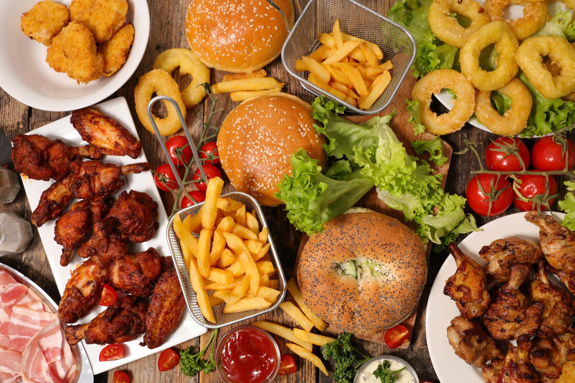 Vue d'une table rustique garnie de hamburgers, de poulet frit, de rondelles d'oignon, de frites et de tranches de tomates.