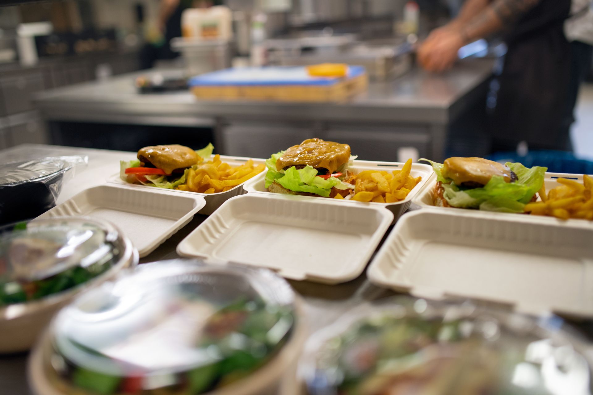 Barquettes de plats à emporter contenant des hamburgers et des frites posées sur le comptoir d'une cuisine professionnelle.