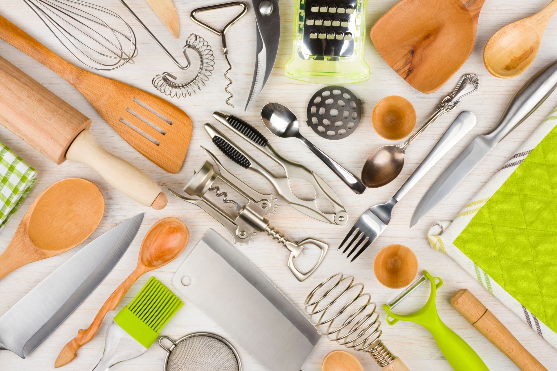 Une disposition de cuillères en bois, rouleau à pâtisserie, fouet, couteau et un éplucheur, sur une table.