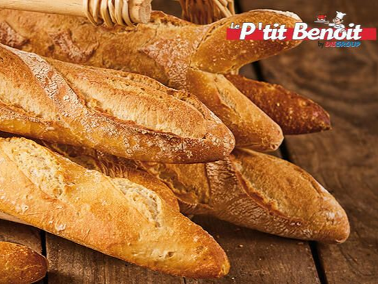 Gros plan sur plusieurs baguettes françaises dorées empilées sur une surface en bois foncé.
