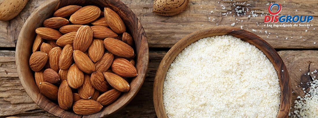 Deux bols en bois posés sur une surface rustique : l'un rempli d'amandes entières et l'autre de noix de coco râpée.