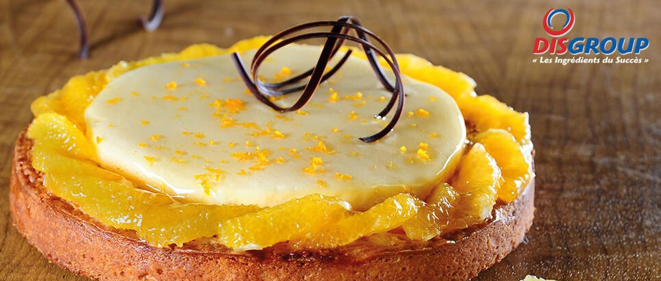 Une tarte ronde aux fruits garnie de tranches d'orange, d'un disque de crème et de copeaux de chocolat.