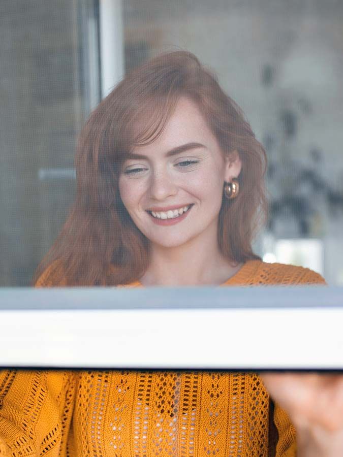 Femme fermant une fenêtre avec moustiquaire