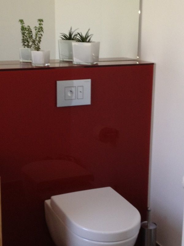 Weiße Toilette vor einer roten Glaswand