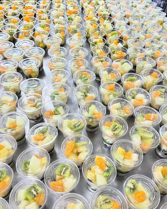 Un montón de vasos de plástico llenos de fruta sobre una mesa.
