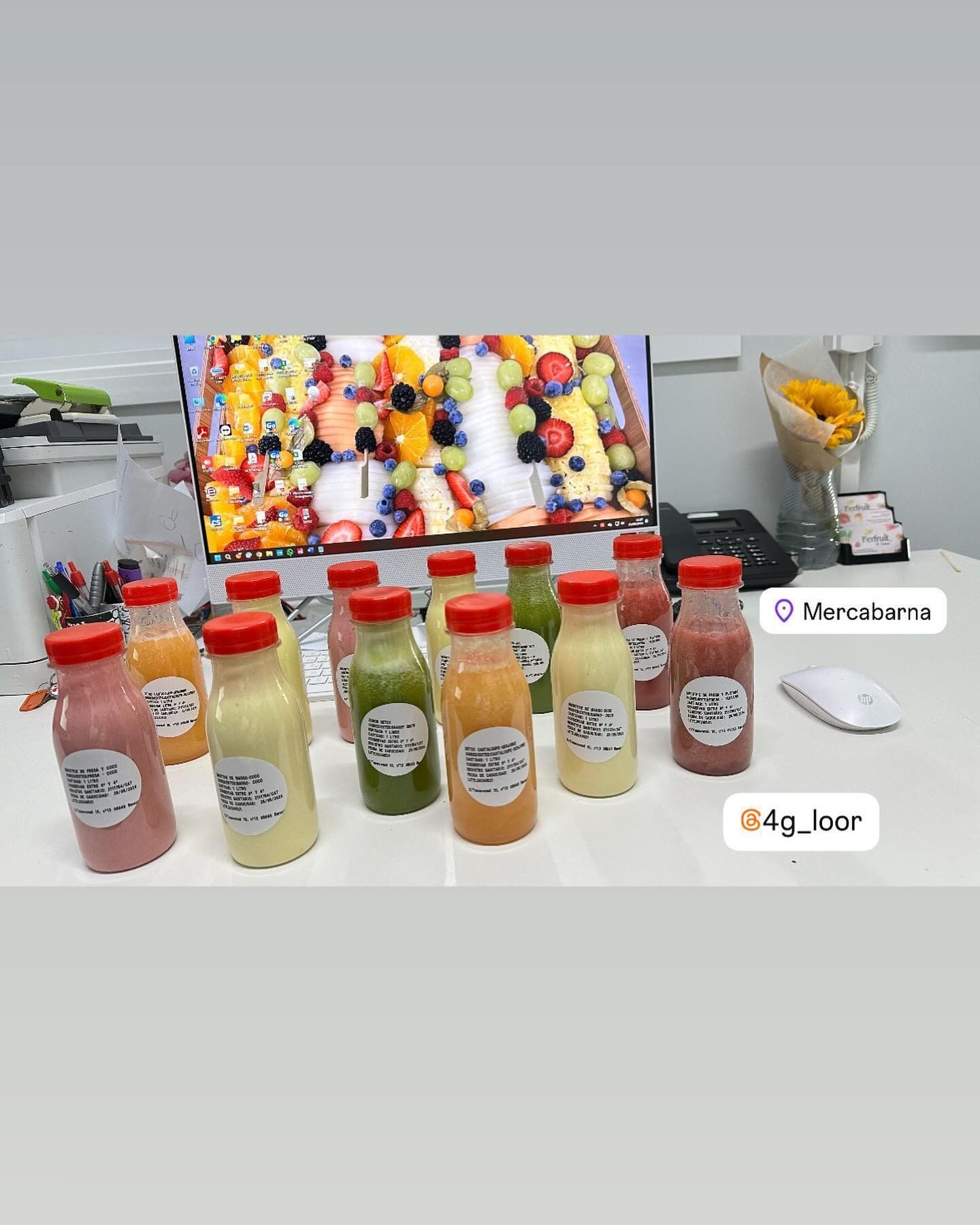 Un montón de botellas de jugo están sobre una mesa frente a un monitor de computadora.