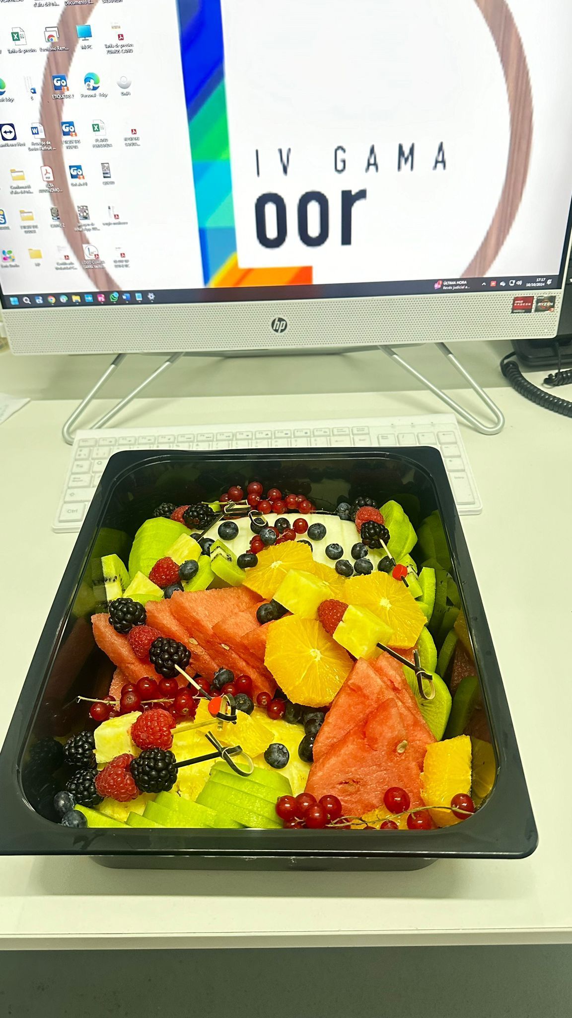 Un tazón de ensalada de frutas está sobre un escritorio frente a una computadora.