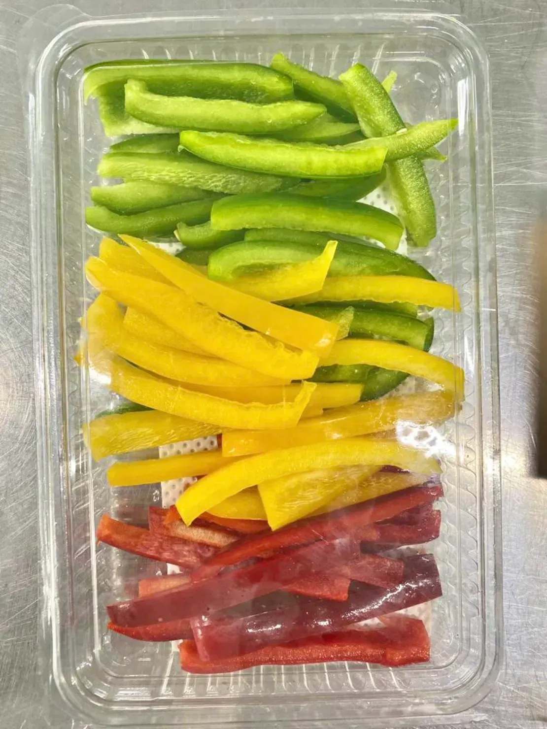 Un recipiente de plástico lleno de pimientos cortados en rodajas de diferentes colores.