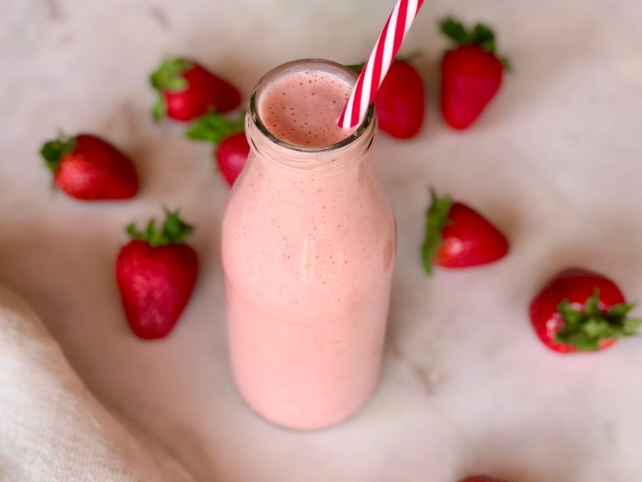 Un batido de fresa en una botella con fresas en el fondo.