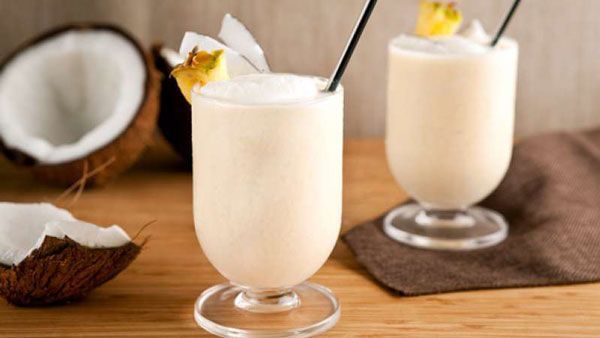Dos vasos de leche de coco con pajitas en una mesa de madera.