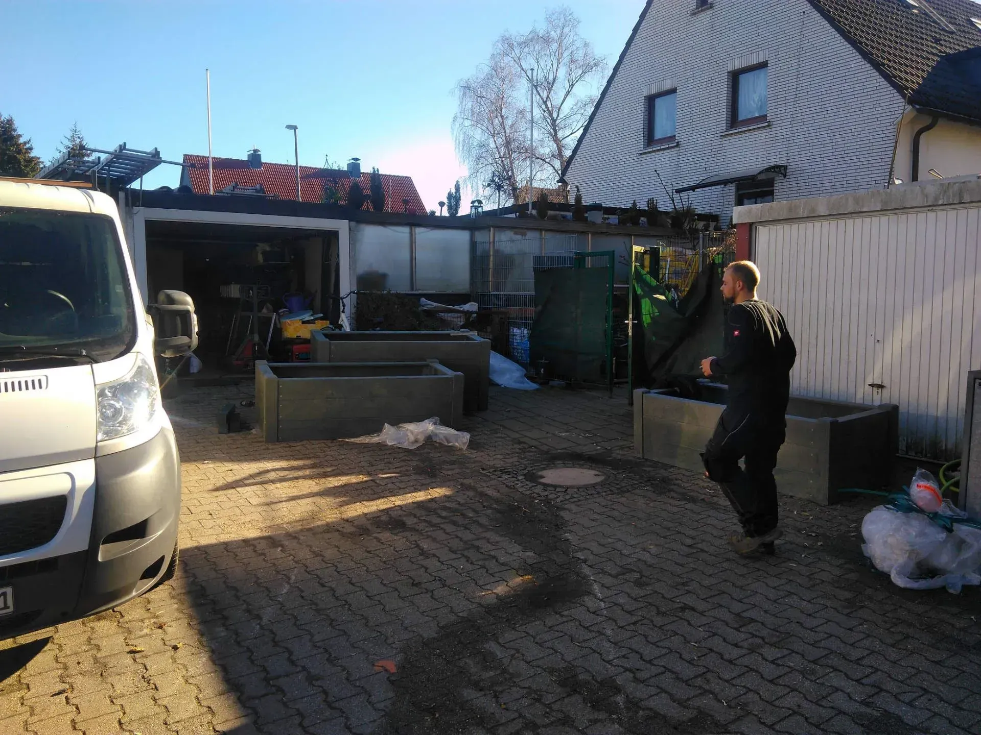 Ein Mann steht in einer Einfahrt vor einem weißen Lieferwagen und baut Pflanzkästen auf