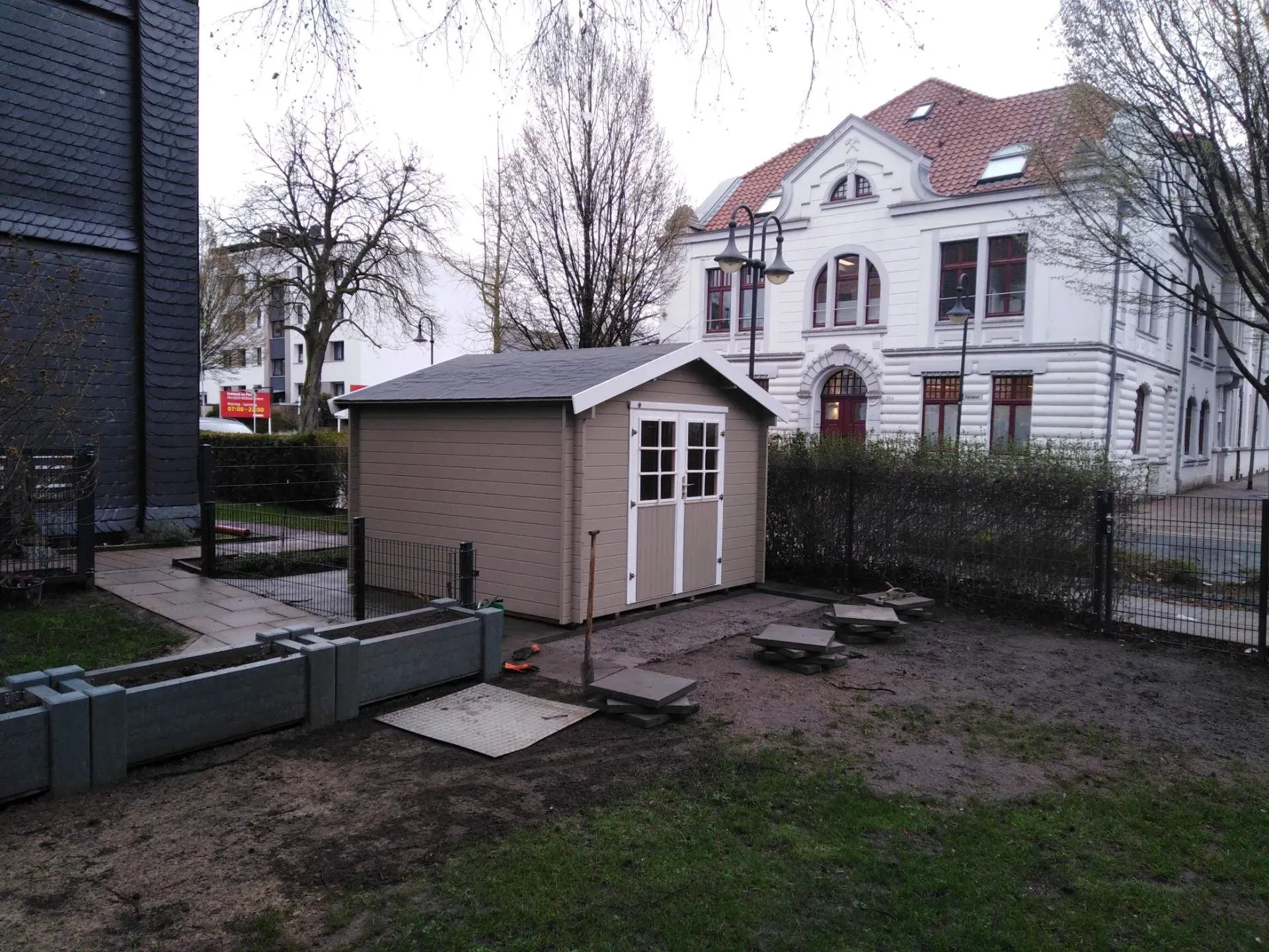 Ein kleiner Schuppen steht mitten in einem Hof, daneben sind hohe Blumenkästen