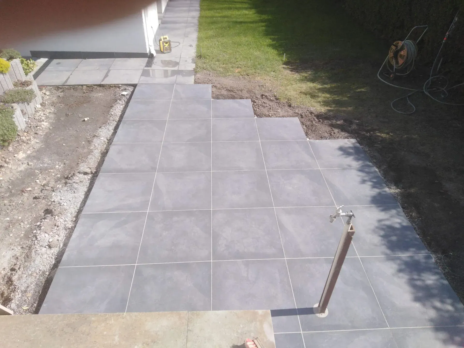 In einem Garten wird eine geflieste Terrasse gebaut.