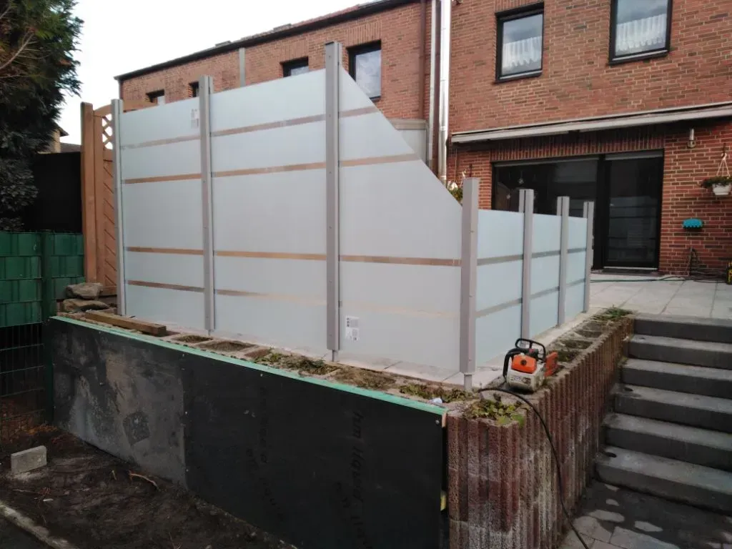 Vor einem Backsteinhaus wird ein Glaszaun errichtet.