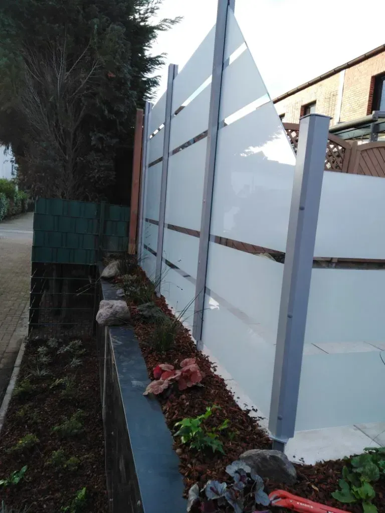 Ein Glaszaun mit Milchglas-Streifen und einem Beet davor