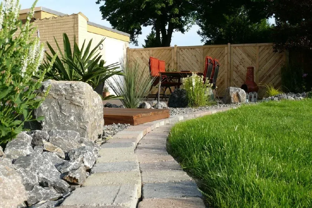 Ein üppiger grüner Rasen mit einem Holzzaun im Hintergrund, vorne ist ein Steinbeet