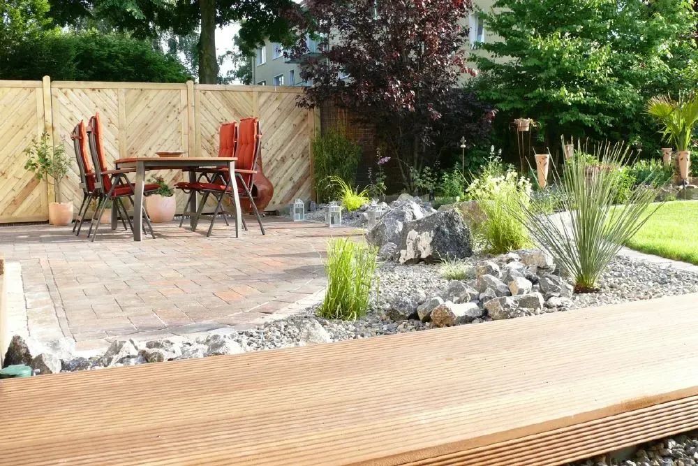 Eine Terrasse mit Tisch und Stühlen und einem Holzzaun, sowie einem Steinbeet