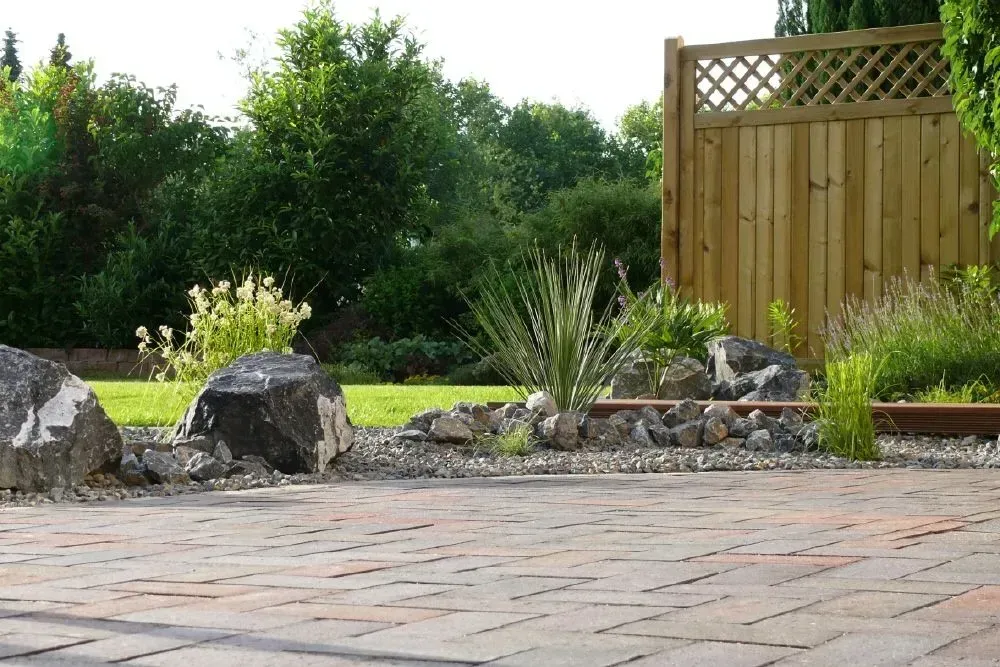 Eine geflieste Terrasse mit einem Holzzaun im Hintergrund und Pflanzen