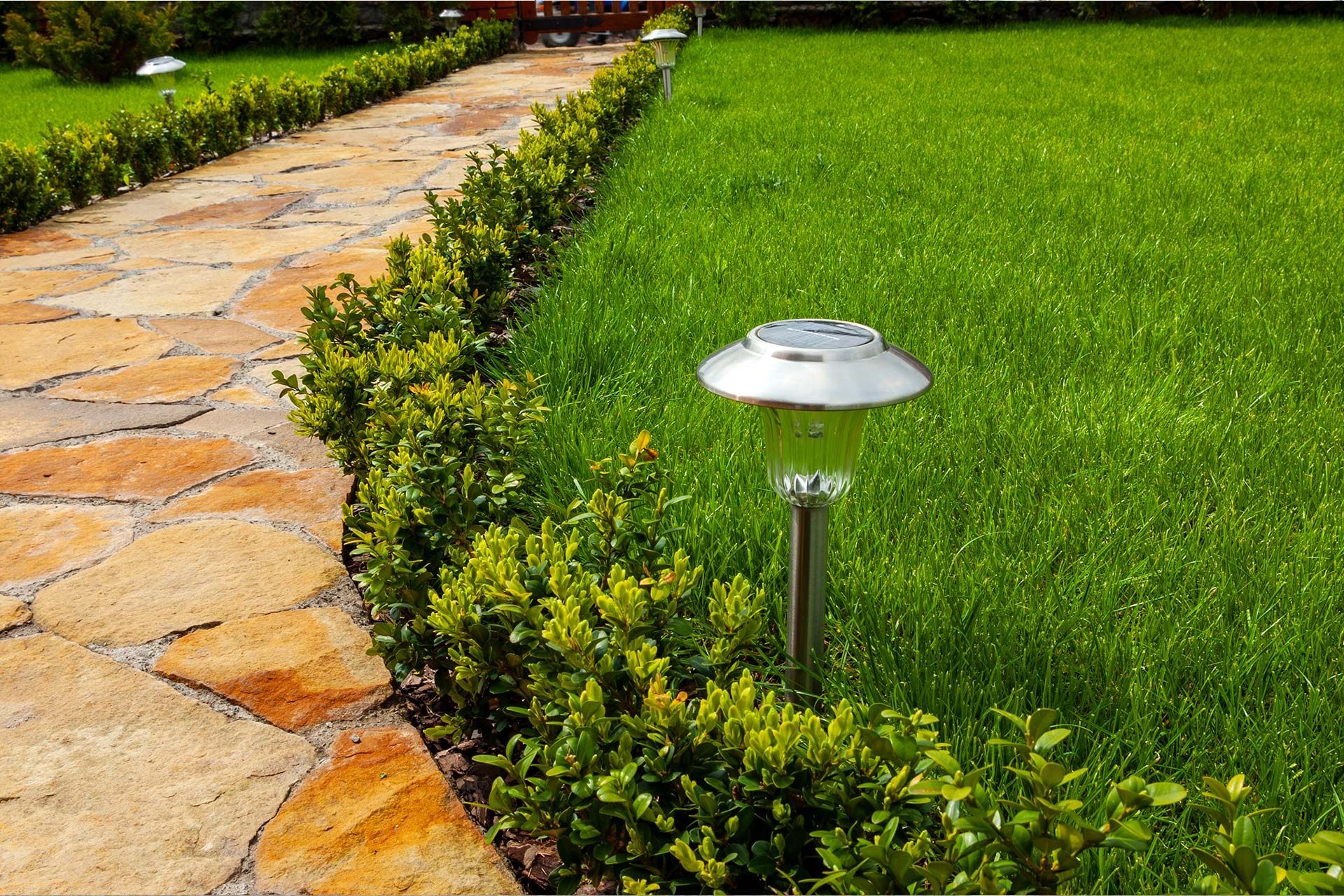 Ein Steinweg, der zu einer Wiese führt, an deren Seite sich eine Solarleuchte befindet.