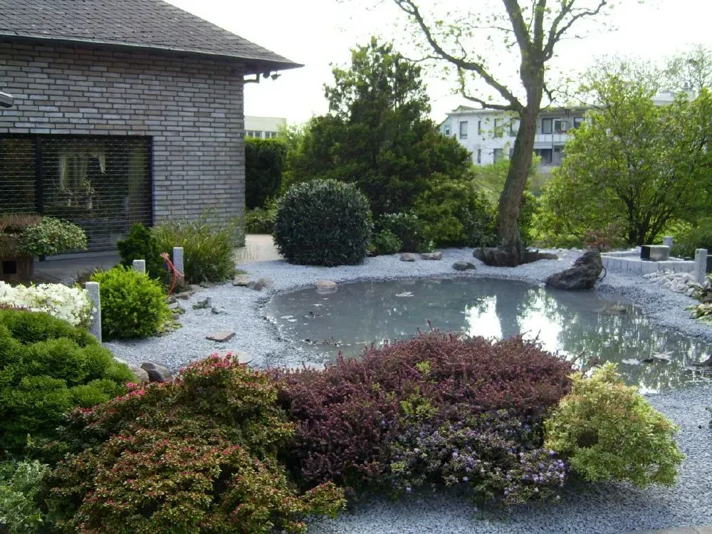 Ein Backsteinhaus mit einem Teich, mit hellgrauen Steinen und Büschen davor