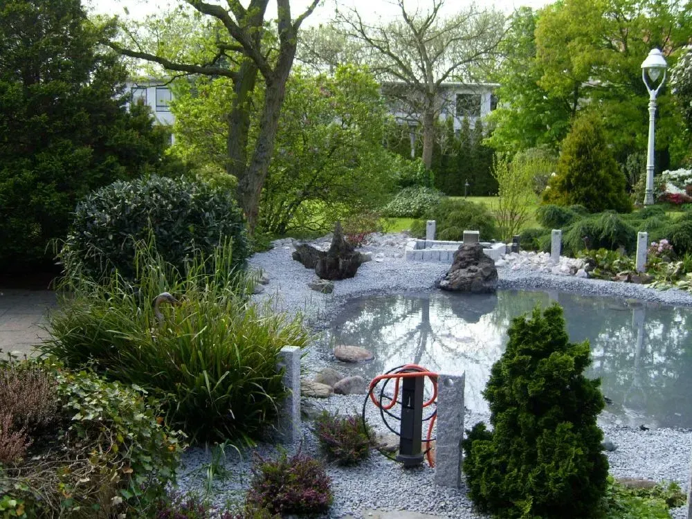 Ein Teich, umgeben von Steinen, Bäumen und Sträuchern in einem Garten