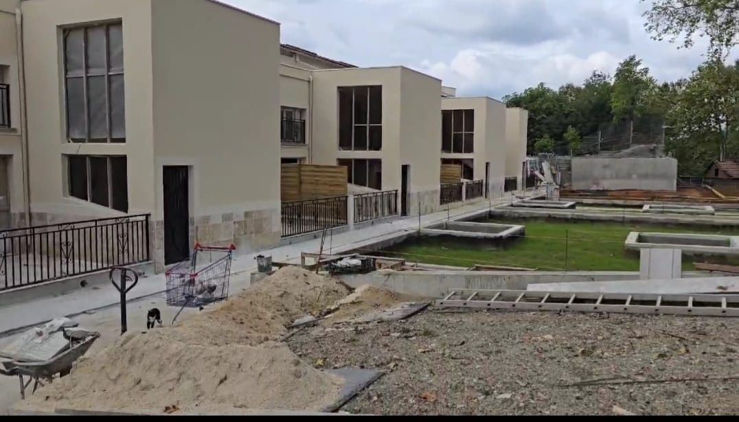 Hilera de edificios color beige en construcción, con ventanas abiertas y una pasarela. Materiales de construcción en primer plano.