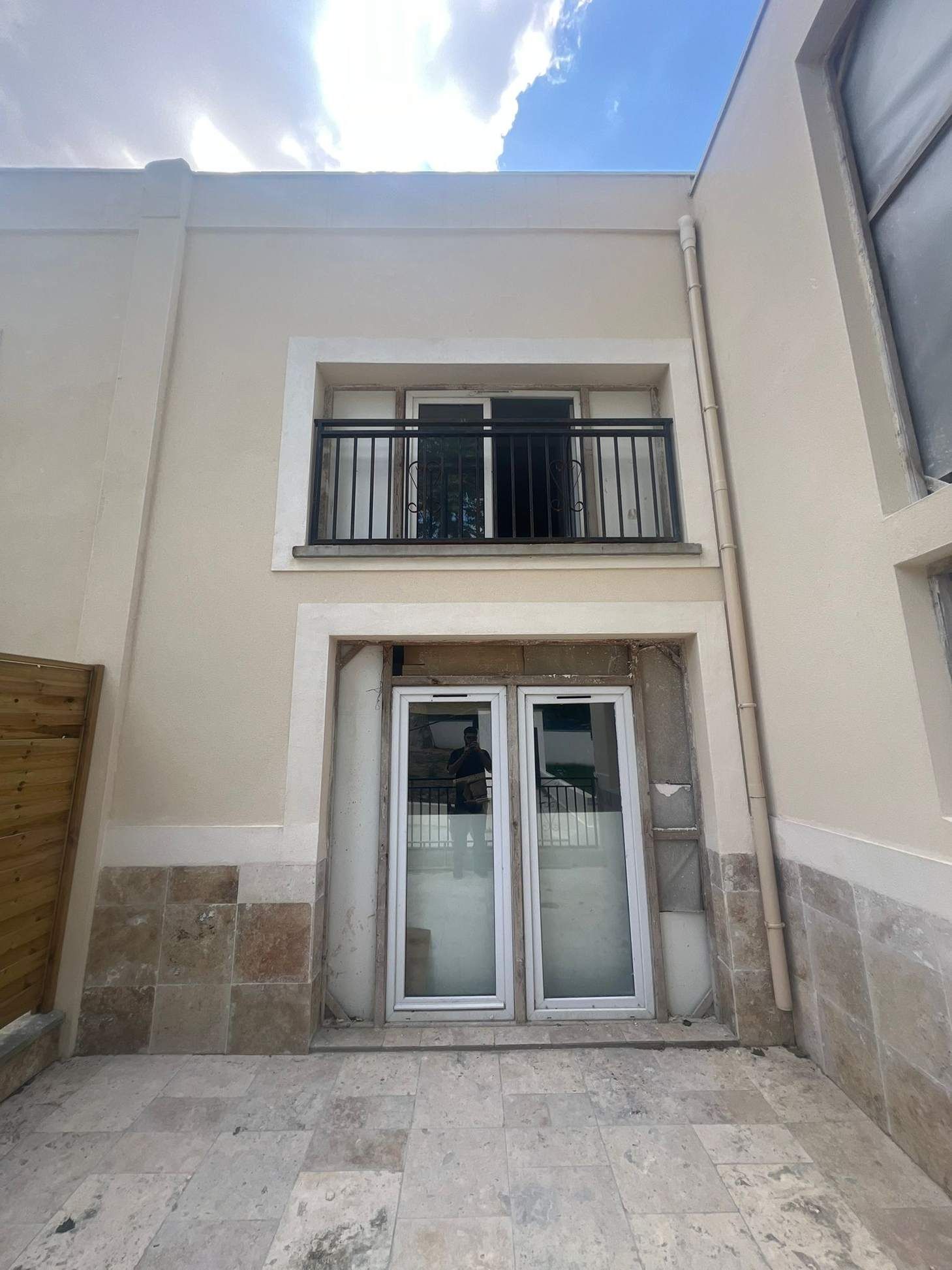 Edificio color beige con balcón y puertas de cristal. Cielo nublado. Patio de piedra en primer plano.