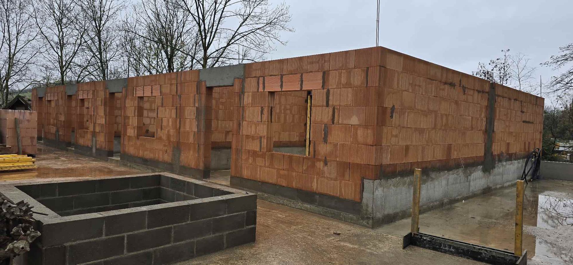 Zona en construcción con una estructura de ladrillo parcialmente construida, aberturas para ventanas y una pequeña piscina.